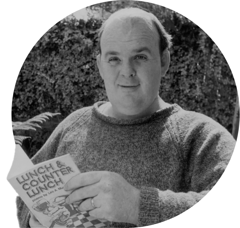 A black and white image of a young Les Murray he is holding a book of his poetry and standing in a garden